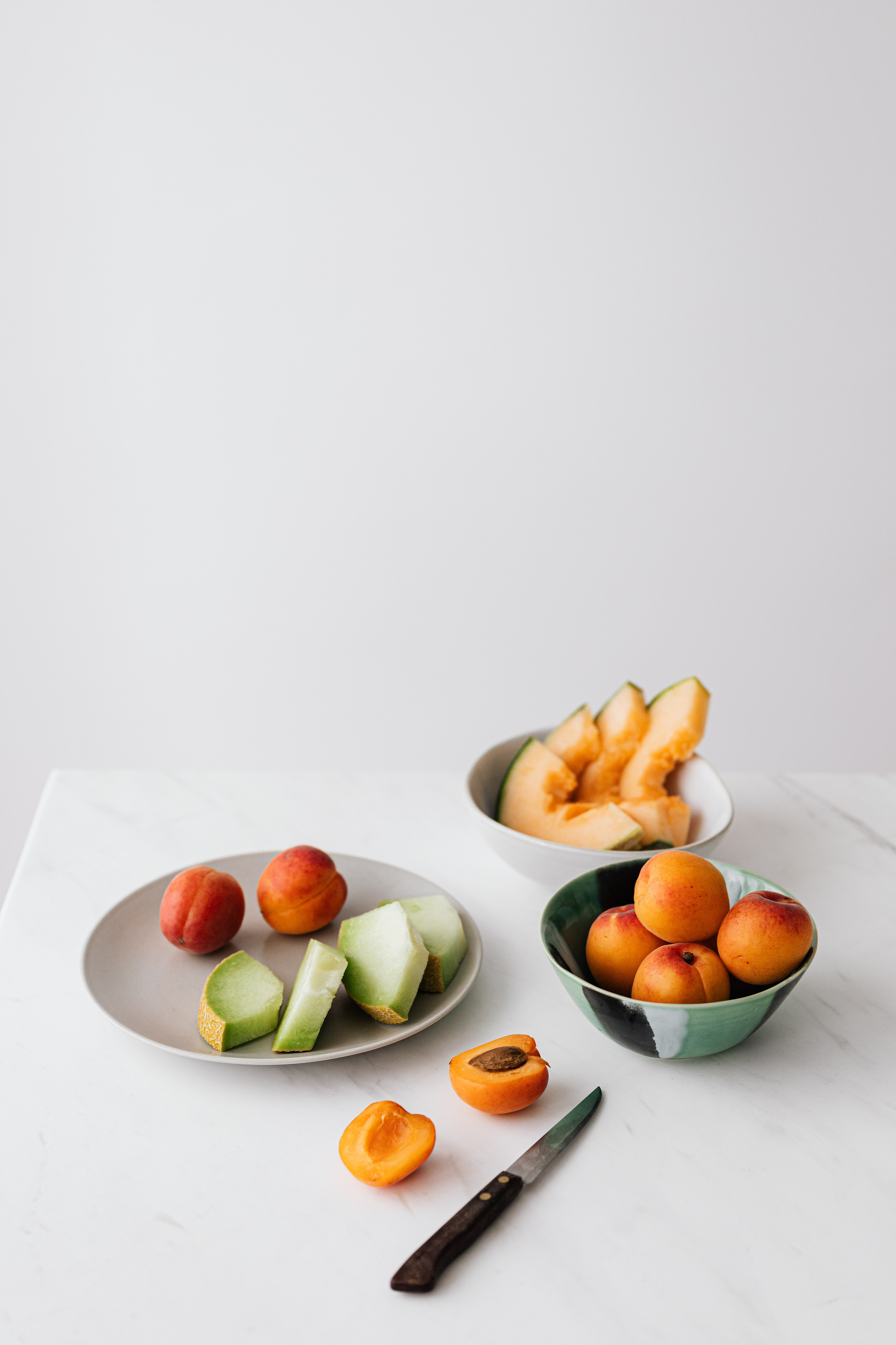 Bowl with mixed healthy fruits placed on table with halved apricot and knife